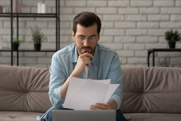 istock Pensive Caucasian man work on laptop reading paper documents 1270316195