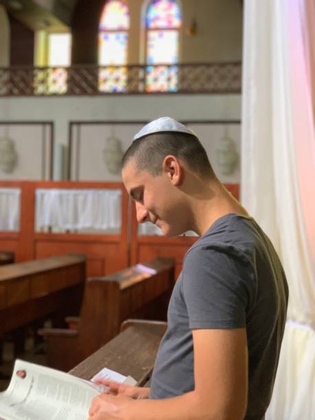 A male teenager in a synagogue with kippa or yarmulke on his head studying the Torah in lateral view. A male teenager in a synagogue with kippa or yarmulke on his head studying the Torah in lateral view. yarmulke photos stock pictures, royalty-free photos & images