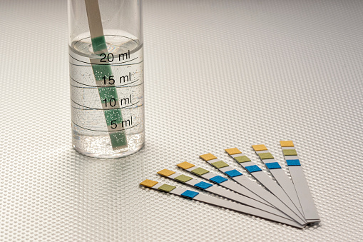 close up of ph analysis strips with a strip inserted in a graduated tube with water, on a rough metal surface