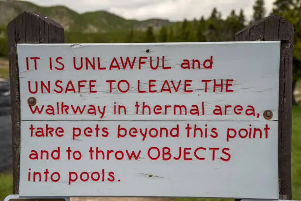 Photo of Sign along the geyser hot springs boardwalks in Yellowstone National Park reminding hikers to stay on the trail and not throw trash into the thermal pools