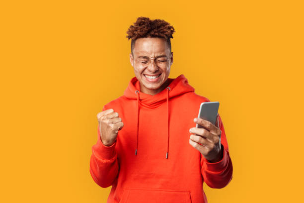 Young adult guy holding modern smartphone and rejoiced stock photo