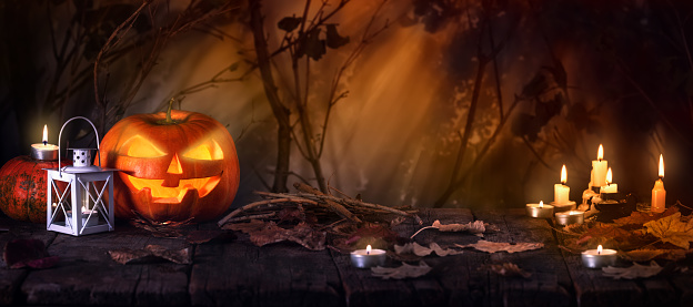 Halloween pumpkins on old wooden table. Jack O’ Lanterns with candles in spooky forest with ghost lights. Halloween Background or banner.