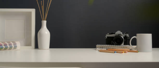 Close up view of worktable with stationery, camera, supplies, mock up frame and decoration in home office