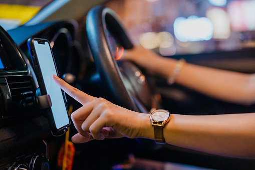 Shot of an Asian woman E-hailing driver wearing face mask, using smartphone for direction and receive passenger order