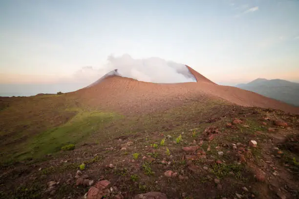 Photo of scenic panorama of the active volcano Telica with the first light of dawn and sulfuric smoke rising from the volcanic cone