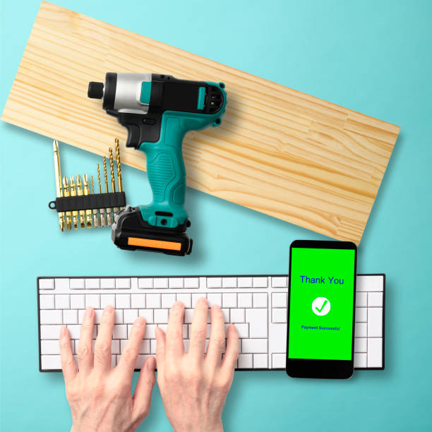 Cordless screwdriver and plank bought with a cashless payment using a smart phone on light blue background.