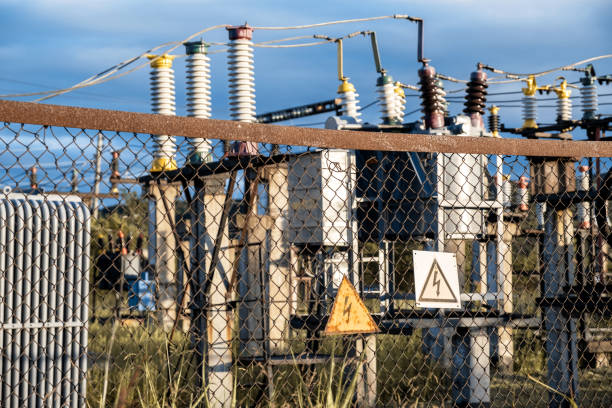 Electrical hazard signs on the metal grid. Against the background of a defocused high-voltage electrical substation. Risk of electric shock.
