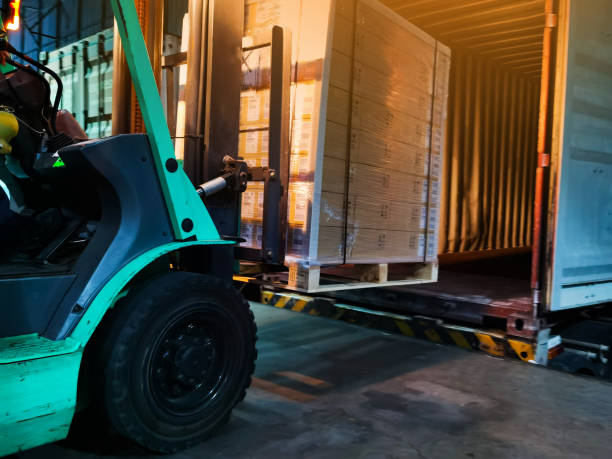 istock Worker driving forklift loading shipment carton boxes goods on wooden pallet at loading dock from container truck to warehouse cargo storage in freight logistics, transportation industrial, delivery 1270360263
