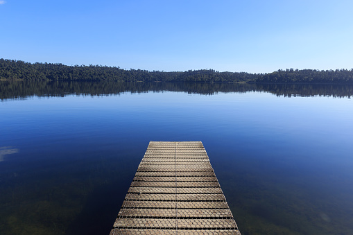 Wooden pier in the morning at calm mirror lake with mountain background in New Zealand.