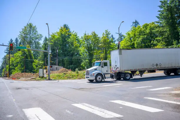 Photo of Local big rig semi truck with dry van semi trailer standing on the city crossroad intersection with red traffic light