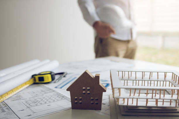 istock Engineer is holding a helmet standing in his office and has a blueprint and model on his desk. 1270368398