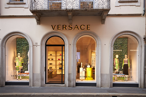 Illuminated showcase of Versace store. Front door to the store. Mannequins in fashionable clothes are on display. Milan Italy 08.2020