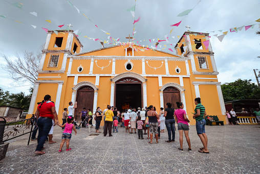 Ometepe Island / Nicaragua - July 15, 2019: Wide angle shot of people entering yellow church in Moyogalpa village