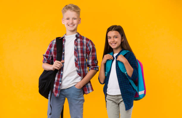 istock Casual schoolchildren standing with backpacks on yellow studio 1270374405