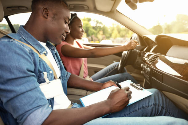 istruttore maschio che esamina donna nera alla guida di un'auto - driving test foto e immagini stock