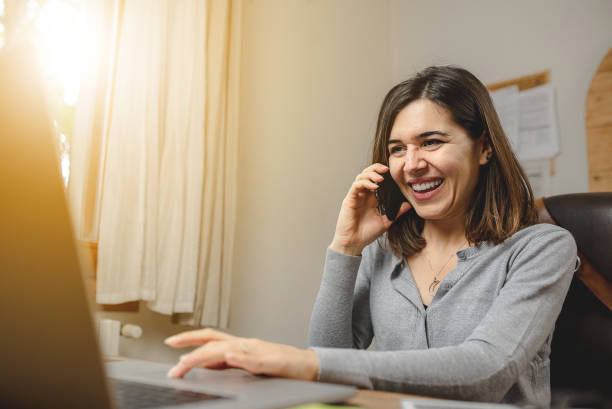 istock woman talking on the phone while working on computer and smiling. Desk Offie and browsing concept. 1270376062