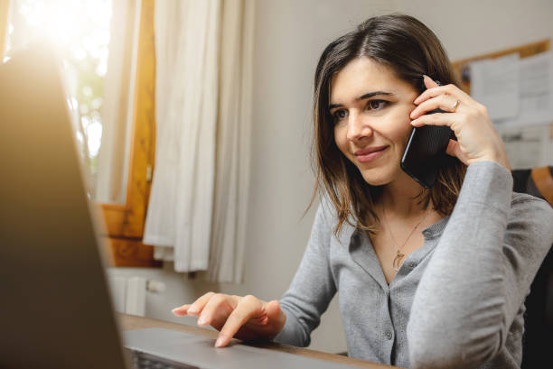 istock woman talking on the phone while working on computer and smiling. Desk Offie and browsing concept. 1270376780