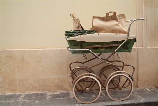 Vintage baby carriage exposed outside a children shop .Ortigia urban area. Syracuse Siracusa, Sicily Italy, summer season