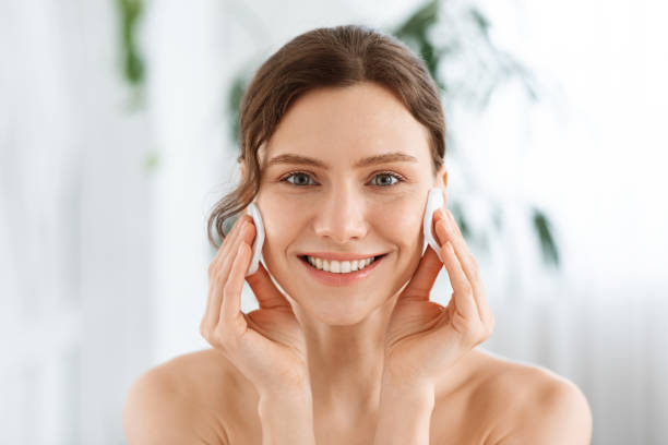 garota alegre segurando almofadas de algodão em suas bochechas - creme de limpeza facial - fotografias e filmes do acervo