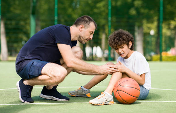 учитель помогает мальчику с травмой колена после игры в баскетбол - child family tutor father стоковые фото и изображения
