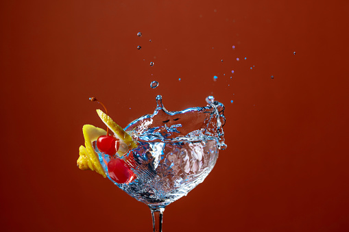 Cocktail splashes. Drink with lemon and cherries. Mixed light, red background.