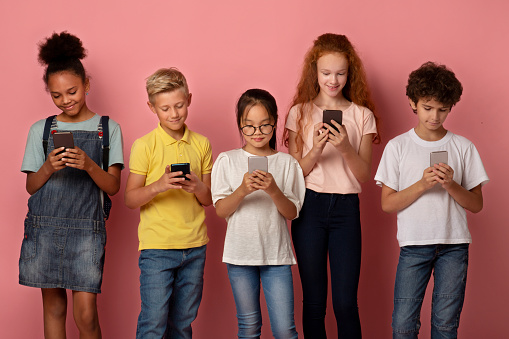 Group of diverse schoolkids stuck in mobile phones studying online over pink background