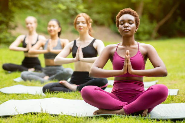 yoga for inner peace. diverse young girls meditating in lotus pose and doing namaste gesture at park - yoga meditating business group of people imagens e fotografias de stock