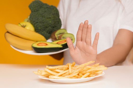 Woman Refusing Plate With Unhealthy Food Choosing Vegetables And Fruits Instead Of French Fries, Yellow Background, Selective Focus, Crop