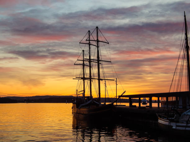 Dark ship in evening harbor. Beautiful sky with red clouds. Golden water reflections. Oslo, Norway.