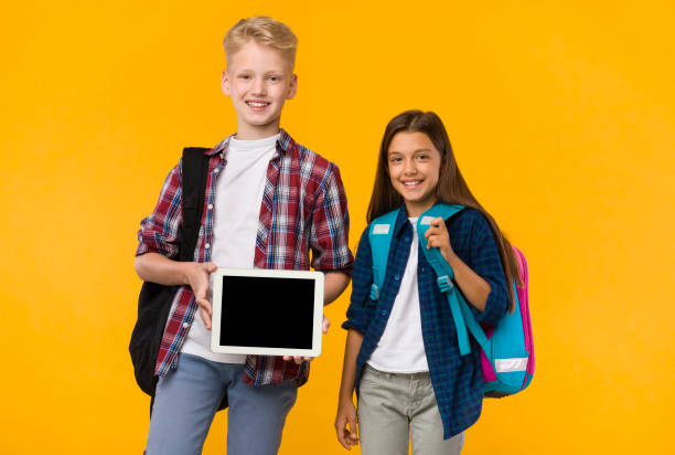 istock Smiling school boy and girl showing tablet screen at camera 1270394928