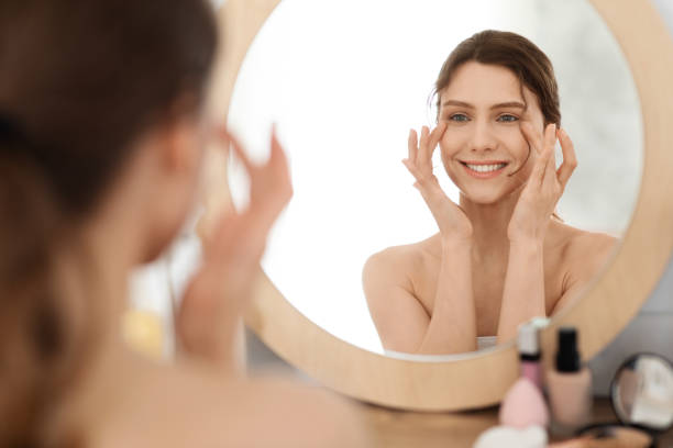 junge frau massiert augenzone, blick auf spiegel - human face rubbing women beauty treatment stock-fotos und bilder