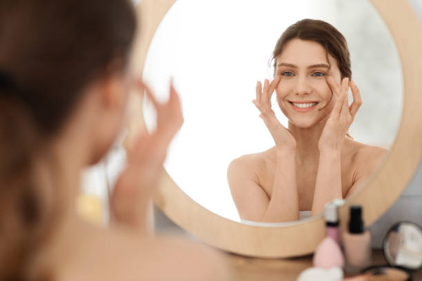 istock Young woman massaging eye zone, looking at mirror 1270395049