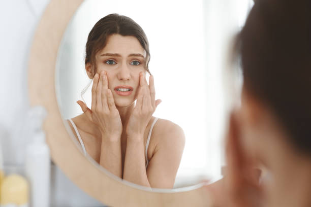 Stressed girl touching her skin and looking at mirror First wrinkles. Stressed girl touching her skin and looking at mirror at home stress acne stock pictures, royalty-free photos & images