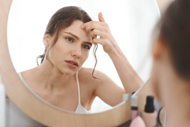 istock Sad girl touching pimple on her forehead, looking at mirror 1270395068