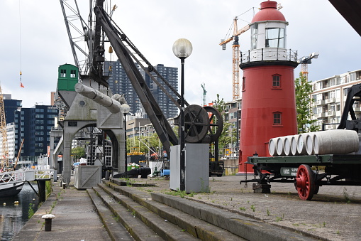 Rotterdam, Netherlands - June 19, 2020: Some of showpieces of the national maritime museum in Rotterdam exhibited outside. On the picture are red lighthouse, harbor crane and wheeled car near canal.