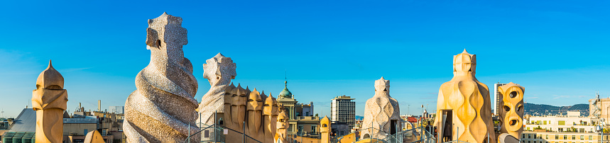 Tourists exploring Gaudi's iconic chimneys and ventilation towers on the rooftop of Casa Mila, La Pedrera, under blue summer skies, Barcelona, Spain.