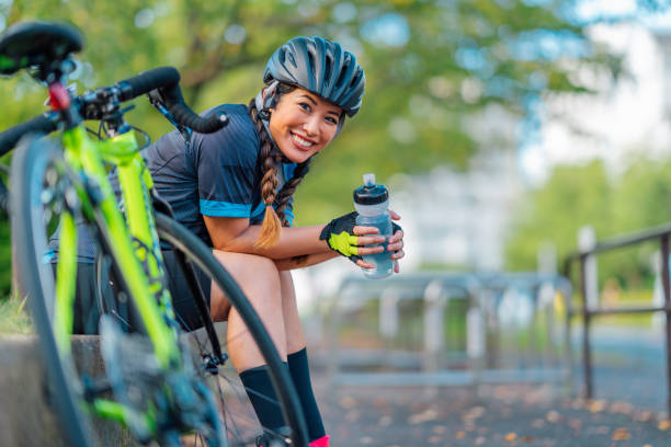 verticale du vélo féminin souriant pour l’appareil-photo dans le stationnement public - faire du vélo photos et images de collection