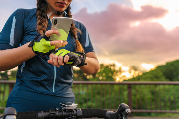 ciclista donna che alleva il suo orologio intelligente e lo smartphone prima di andare in bicicletta - gps watch foto e immagini stock