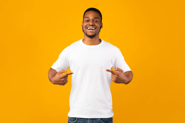 african man pointing at himself standing in studio, yellow background - one man only imagens e fotografias de stock