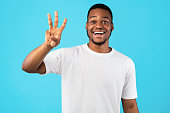 African American Guy Showing Three Fingers Counting Over Blue Background