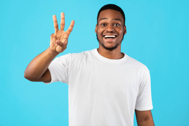 афроамериканец парень показывая три пальца подсчета за синий фон - human finger стоковые фото и изображения