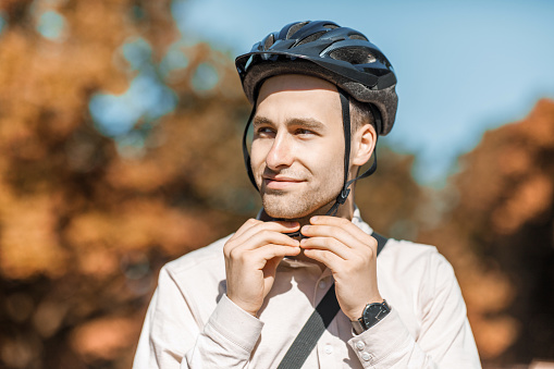 Protection at driving. Attractive young guy puts on safety helmet on street, copy space