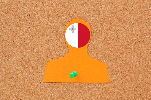 Paper silhouette of male pushpined to cork bulletin board with maltese flag on his head