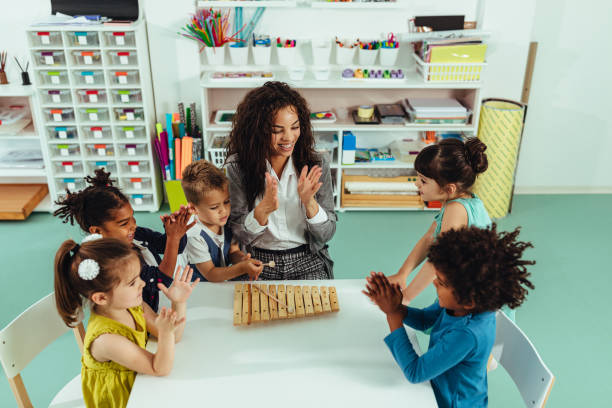 Teacher helping young preschool kids playing musical toys Teacher and children playing with musical toys in kindergarten child care stock pictures, royalty-free photos & images