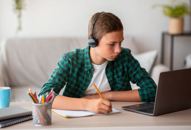 istock Pensive school boy with earphones studying online from home 1270406709
