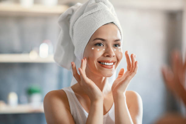 Portrait of pretty lady applying cream under her eyes near mirror indoors Portrait of lovely lady applying cream under her eyes near mirror indoors moisturizing cream stock pictures, royalty-free photos & images