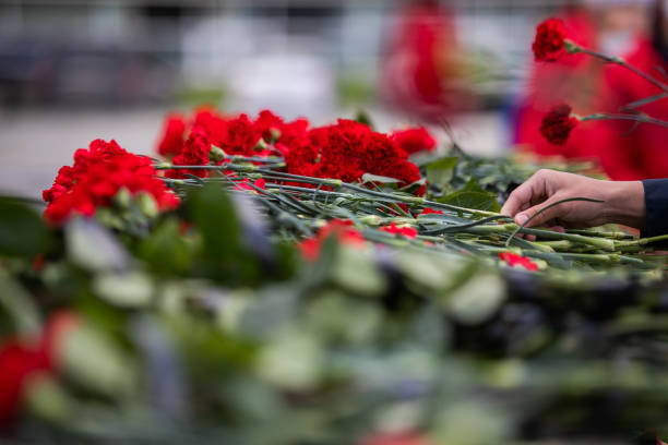 istock A hand puts red carnations on a granite gravestone. Memory of the dead 1270407819