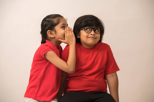 siblings in red  whispering in each other's ears - segredo criança imagens e fotografias de stock