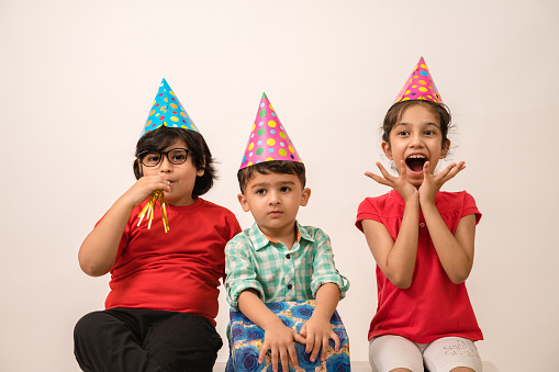 Little kids enjoying the birthday party wearing caps , having fun, blowing whistles