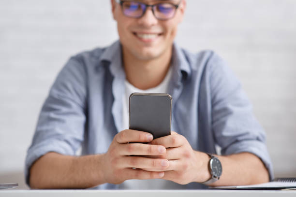 istock Smiling guy with glasses looks at phone, focus on smartphone 1270408667